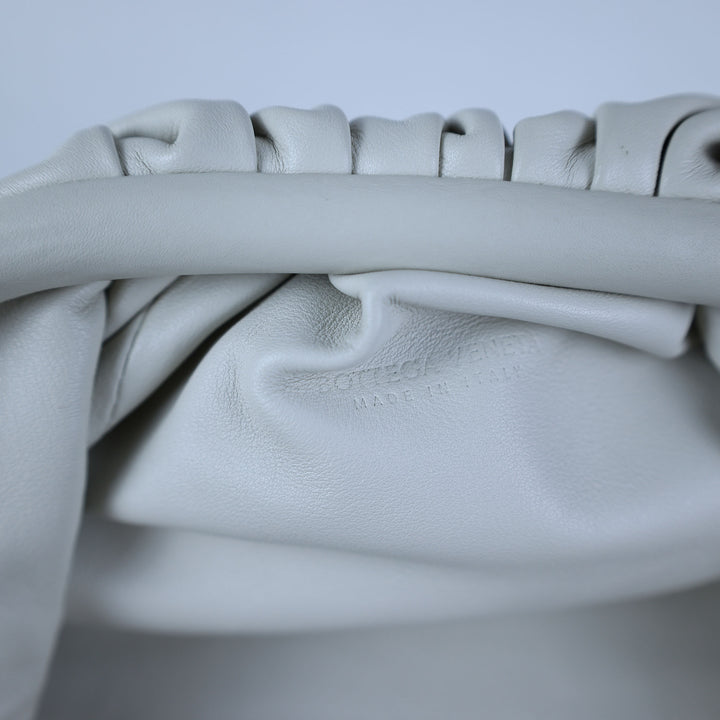 Close-up of a light gray leather bag with visible stitching on a light gray background