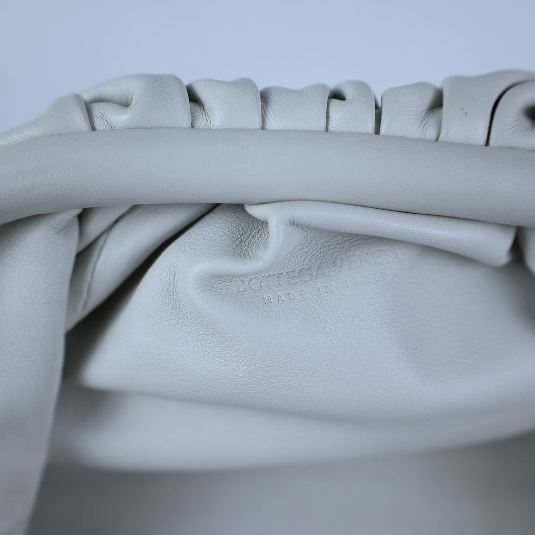 Close-up of a light gray leather bag with visible stitching on a light gray background